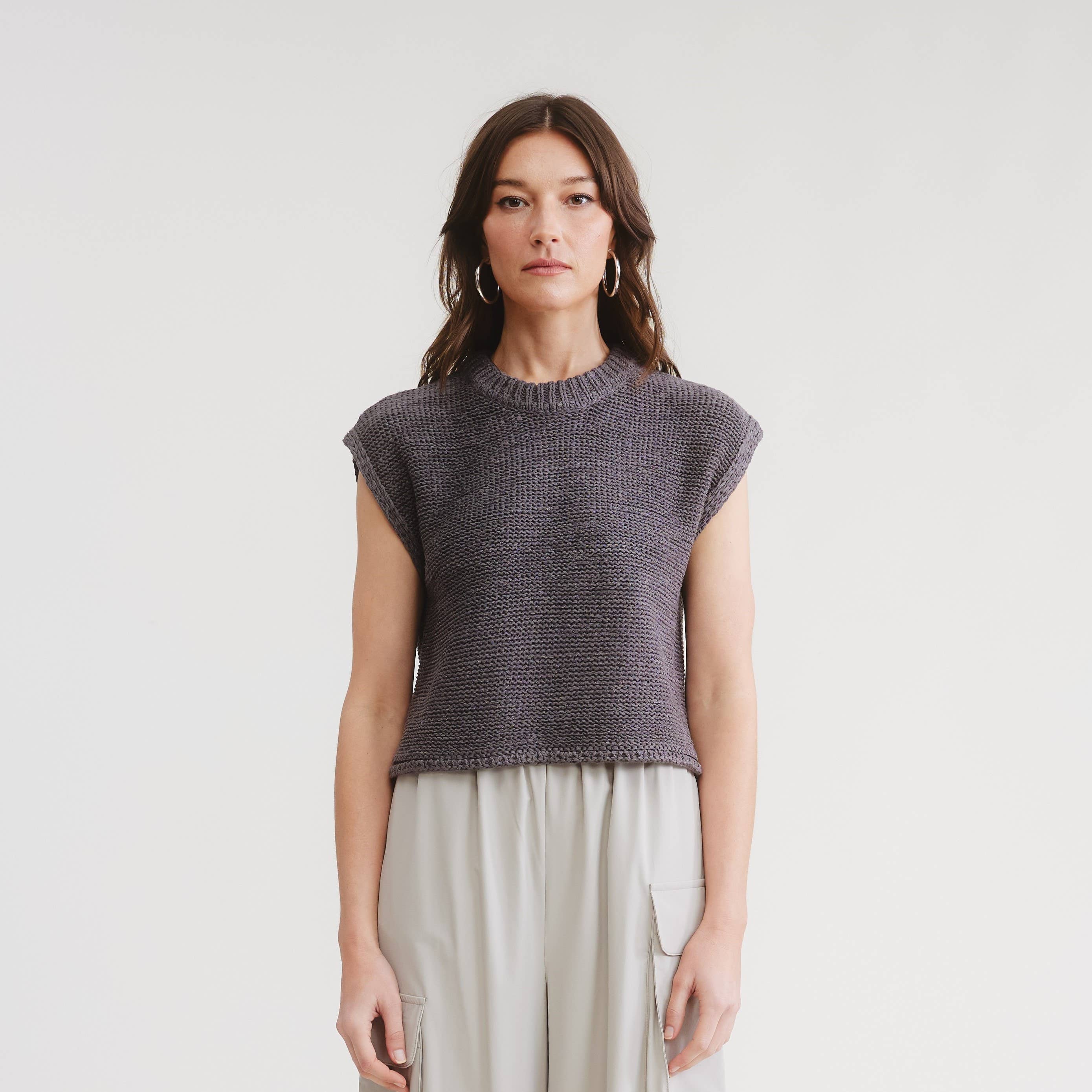 Woman wearing a sleeveless knitted top and light pants on a plain background