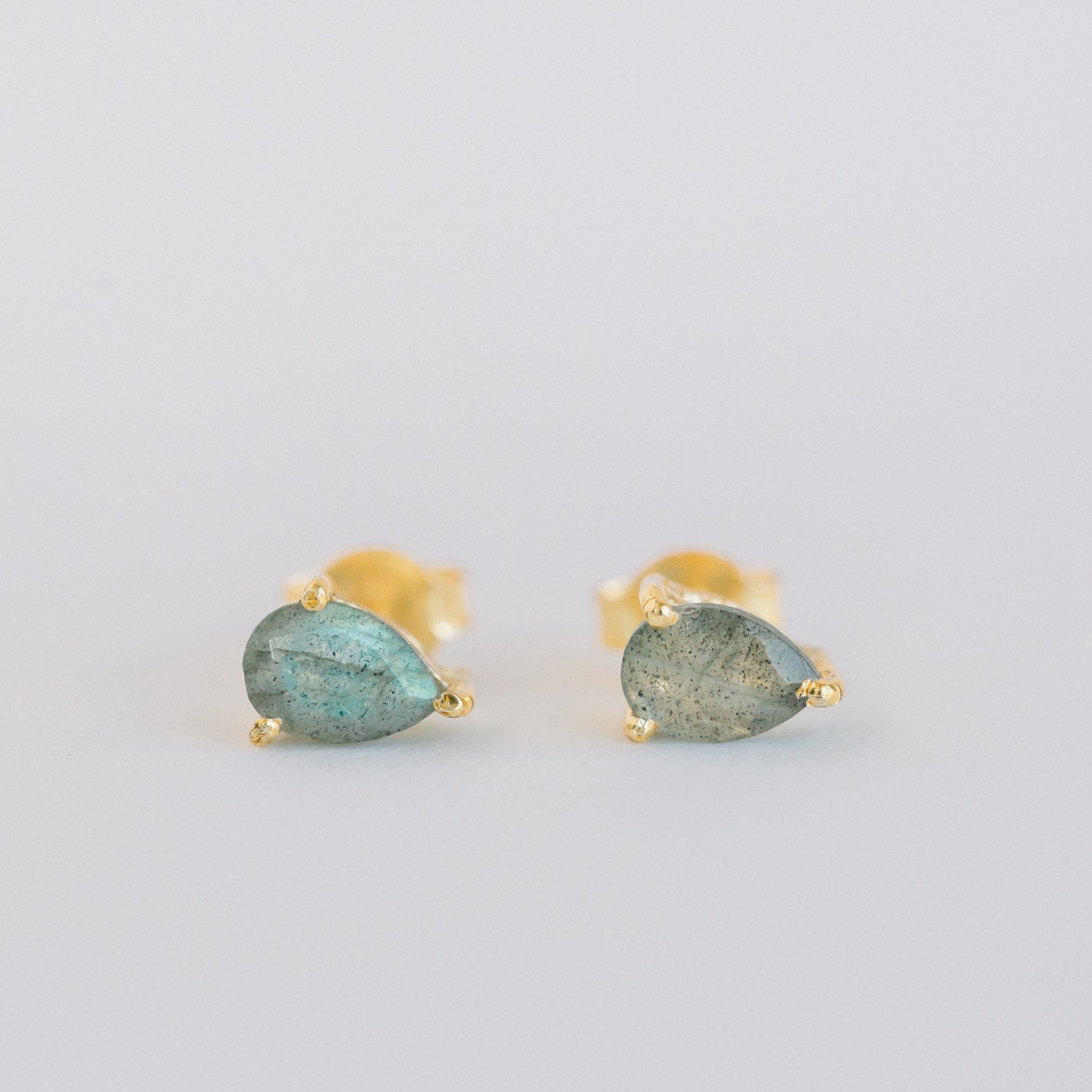 Close-up of elegant labradorite teardrop stud earrings set in 14K gold vermeil displayed on a neutral-toned fabric background. The polished labradorite stones are cut in a teardrop faceted shape, reflecting light for a subtle shine—handcrafted minimalist jewelry made in Vermont from Elli Parr.