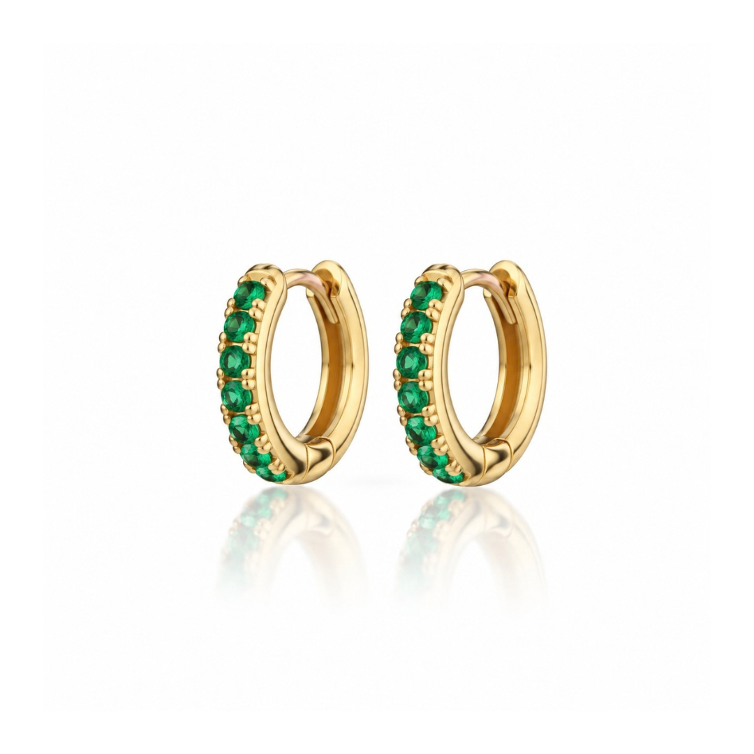 A pair of gold huggie hoop earrings embellished with a row of round-cut green gemstones, displayed on a clean white background with a soft reflection below.